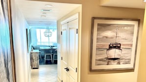 A hallway with a dining area, a framed painting of a boat, and a rustic wooden bowl on a table. - MVG 509 Oceanfront Club floor (North Myrtle Beach)