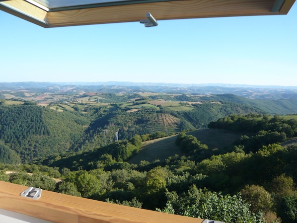 Ein weiter Panoramablick von erhöhter Position, vermutlich einem Balkon, auf ein üppiges Tal mit dichten Wäldern und sanften Hügeln.