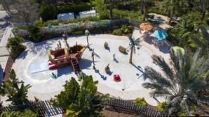 Un espace de jeux aquatiques avec des toboggans et une structure de jeu en forme de bateau de pirate, le tout entouré de palmiers et d’une clôture.