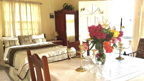 A hotel room with two beds, a dining table with a vase of flowers, and a view of the outside. - Willies Court apartments (St. John)