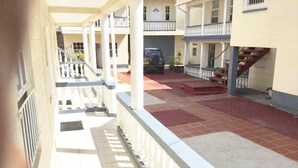 A covered outdoor area with a tiled floor, white railings, and a staircase leading to an upper level. - Willies Court apartments (St. John)
