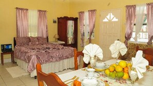A room with a bed, a dining table set with plates, glasses, and a fruit bowl. - Willies Court apartments (St. John)