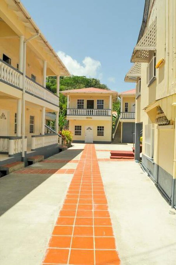 A narrow street with buildings on either side, a central building with a red roof, and a tiled walkway. - Willies Court apartments (St. John)