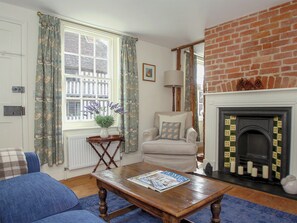 A living room with a fireplace, a blue sofa, a wooden coffee table, and a window with curtains. - What a find in Hollingbourne. (Hollingbourne)
