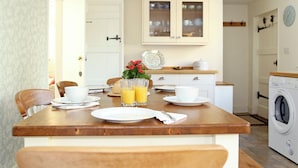 Une cuisine avec une table en bois mise pour le petit-déjeuner, avec des assiettes, des tasses et des verres de jus d’orange.