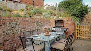 Une terrasse extérieure avec une table dressée pour le repas, entourée de murs en briques et d’une clôture en bois.