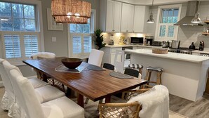 Una cocina moderna con muebles blancos, una mesa de comedor de madera y una lámpara colgante.