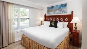 Ein Hotelzimmer mit einem großen Bett, zwei Nachttischlampen, einem fensterbelaubten Fenster und einem Bild an der Wand.