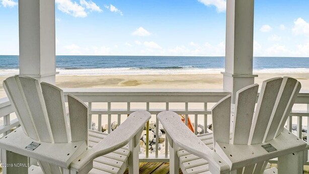 Eine überdachte Terrasse mit zwei Adirondack-Stühlen, die auf einen Strand ausgerichtet sind.