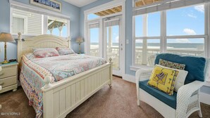 Ein Schlafzimmer mit Bett, Sessel, Deckenventilator und großen Fenstern.