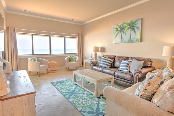 A living room with a sofa, armchairs, a coffee table, and a view of the ocean through large windows.