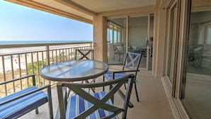 Ein Balkon mit Glastisch und Stühlen mit Blick auf einen Strand.