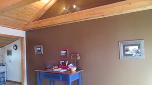 Una habitación con techo de madera, un escritorio con lámpara y cuadros en la pared.
