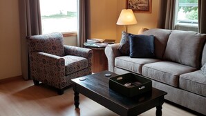 Una sala de estar con un sillón estampado, un sofá, una mesa de centro y una lámpara.