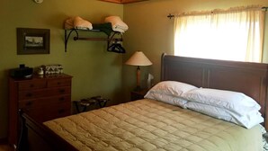 Un dormitorio con techo de madera, una cama con ropa de cama blanca, una mesita de noche con una lámpara y un estante con toallas.