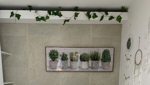 Ein Schlafzimmer mit Bett, Kissen, einer Pflanzenablage und einem Traumfänger an der Wand.