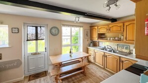 A kitchen with wooden cabinets, a white countertop, a wooden bench, and a door with a doormat. - 2 bedroom accommodation in Binfield, near Newport (Binfield, near Newport)