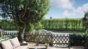 An outdoor patio area with wicker furniture, a glass table, and a view of a hedge and field. - 2 bedroom accommodation in Binfield, near Newport (Binfield, near Newport)