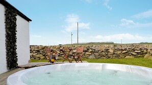 Un bain à remous avec un mur en pierre et un champ verdoyant en arrière-plan.