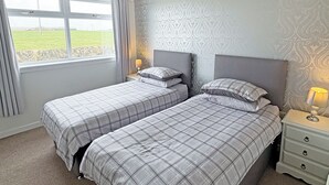 Une chambre avec deux lits, une fenêtre avec des rideaux, un mur à motifs et une lampe de chevet.