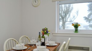 Une table à manger dressée avec des assiettes, des bols, des bouteilles de vin et des verres, un vase rempli de fleurs et une horloge accrochée au mur.