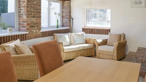 Ein gemütliches Zimmer mit Korbmöbeln, einem Holztisch und großen Fenstern mit Blick ins Freie.