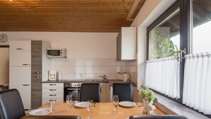 A modern kitchen with white cabinets, a microwave, and a dining area with a wooden table and black chairs. - Beautiful apartment for 5 people with WIFI, TV, terrace and pets allowed (Immerath)