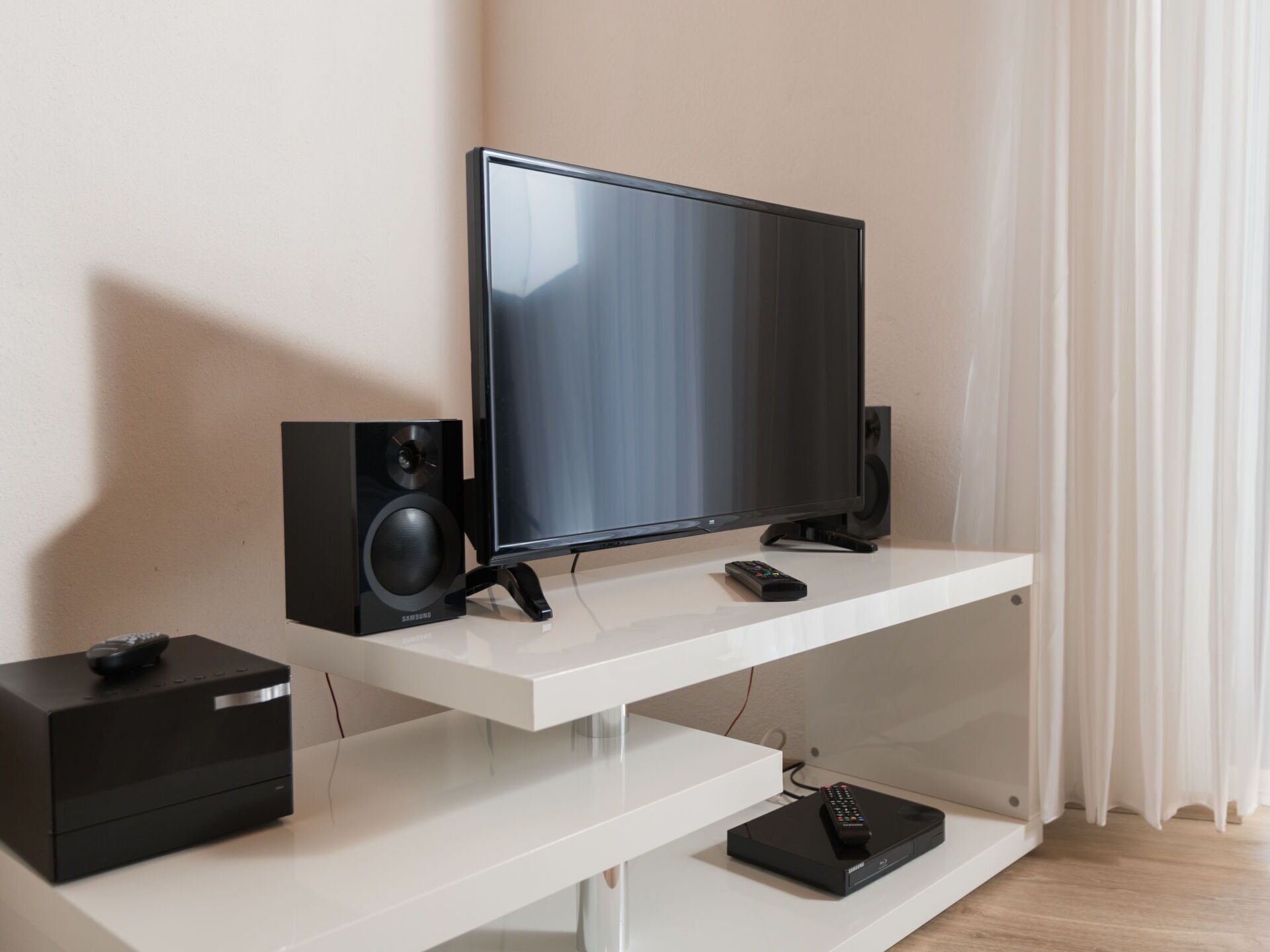Un salon moderne avec un téléviseur à écran plat, deux haut-parleurs noirs, une télécommande et un meuble de rangement noir posé sur une console blanche.