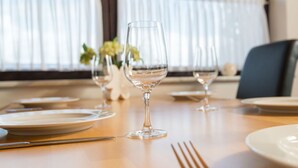 A dining table set with plates, cutlery, and wine glasses, with a window and curtains in the background. - Beautiful apartment for 5 people with WIFI, TV, terrace and pets allowed (Immerath)