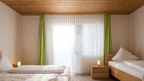 A hotel room with a wooden ceiling, two beds with white bedding, a nightstand with a lamp, and sheer white curtains with green drapes. - Beautiful apartment for 5 people with WIFI, TV, terrace and pets allowed (Immerath)