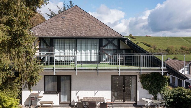 A two-story house with a balcony, stone patio, and outdoor seating area. - Beautiful apartment for 5 people with WIFI, TV, terrace and pets allowed (Immerath)