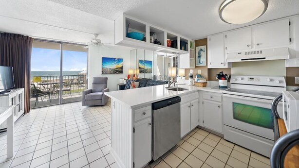 A modern kitchen with white cabinetry, a dishwasher, an oven, and a built-in microwave. There is a balcony with a view of the ocean. - Cozy Condo w/ Gulf Views | Boat-Friendly, Pool, Hot Tub, and Tennis Courts (Gulf Shores)