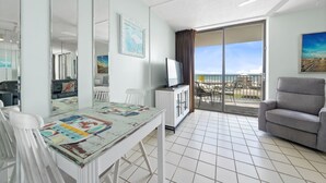 A hotel room with a balcony, a dining area with a table and chairs, a sofa, and a TV on a cabinet. - Cozy Condo w/ Gulf Views | Boat-Friendly, Pool, Hot Tub, and Tennis Courts (Gulf Shores)