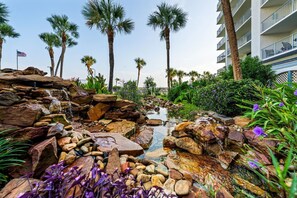 Un espace paysager agrémenté d’un élément aquatique, de palmiers et d’un bâtiment doté de balcons.