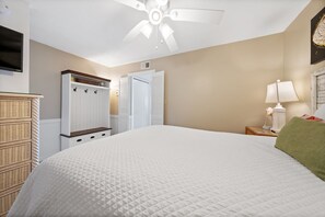 A bedroom with a large bed, a ceiling fan, a wardrobe, a television, and a lamp.