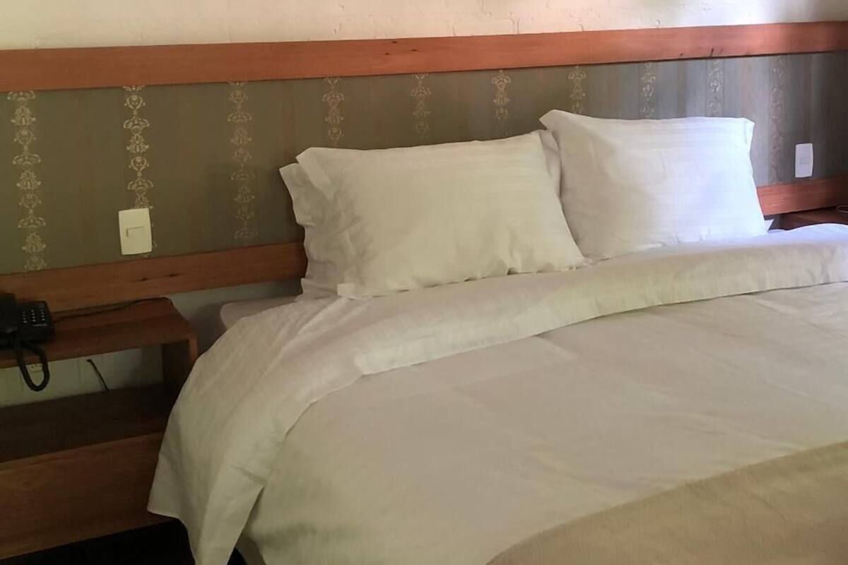 A neatly made bed with white linens, a wooden headboard, and a bedside table with a phone.