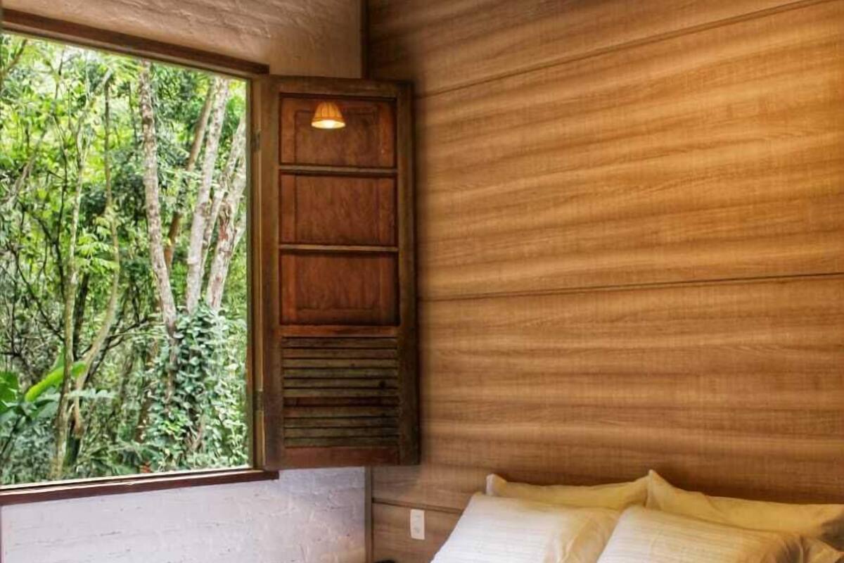A bedroom with a large window, wooden walls, a bed with white linens, and two hanging lights.