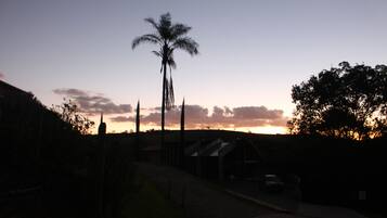 A sunset view with a palm tree silhouette, a paved pathway, and a building with a car parked in front.