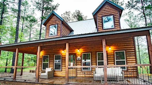 A log cabin with a porch, multiple windows, and a sign that reads "Bear Den."
