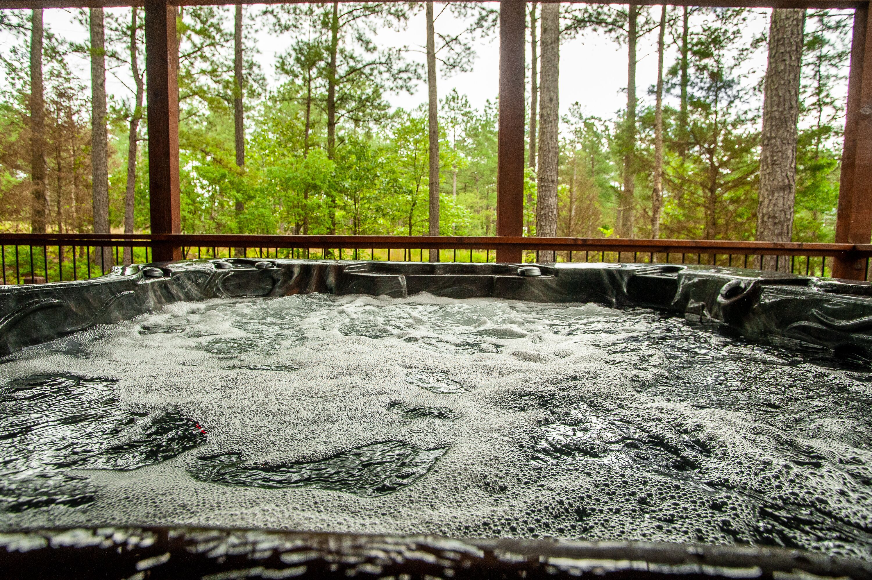 Een hottub met een houten terras en uitzicht op een bos.
