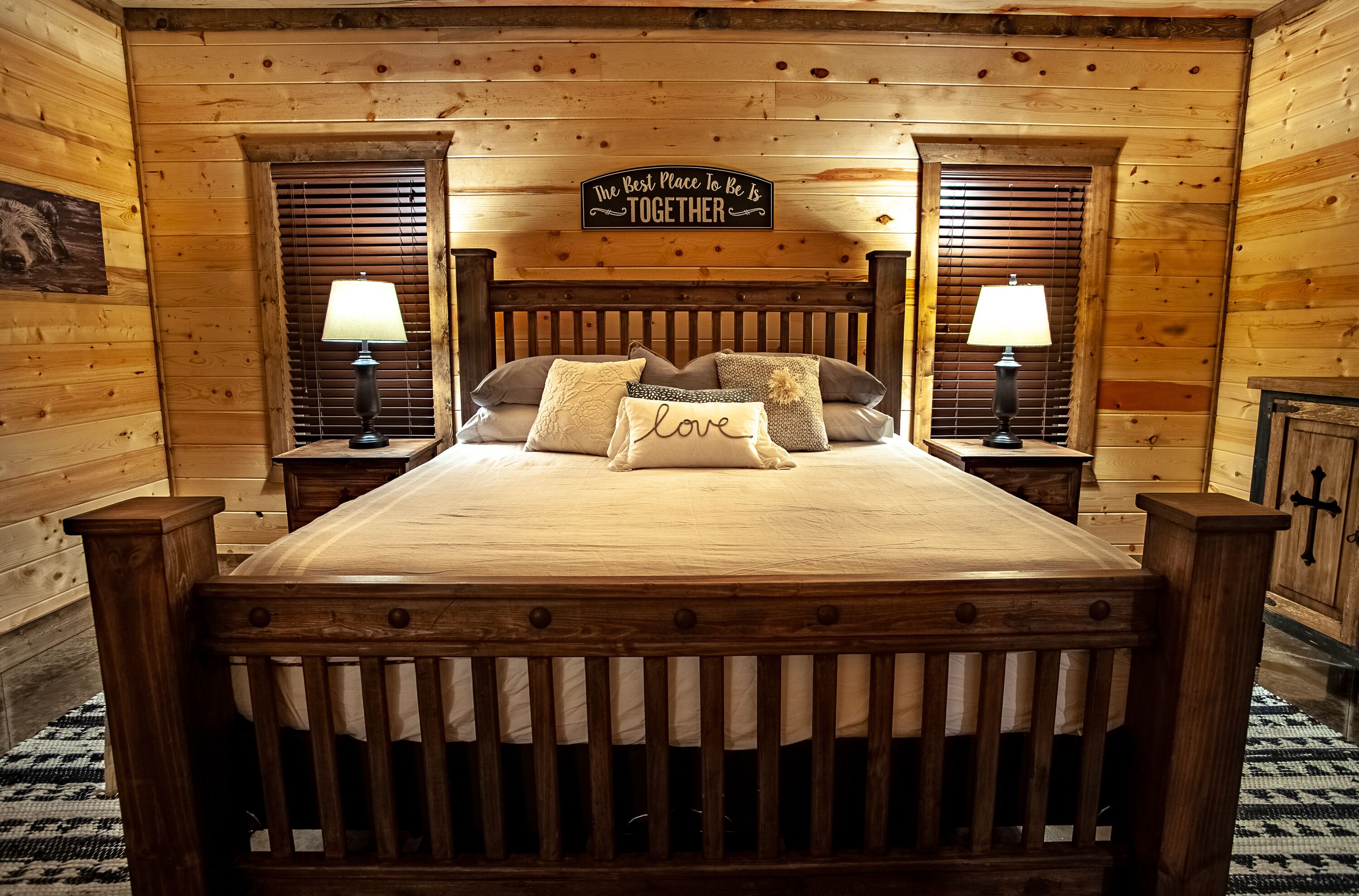 Une chambre à coucher de style cabane en bois, avec un lit, deux tables de chevet, deux lampes et un panneau décoratif au-dessus du lit.