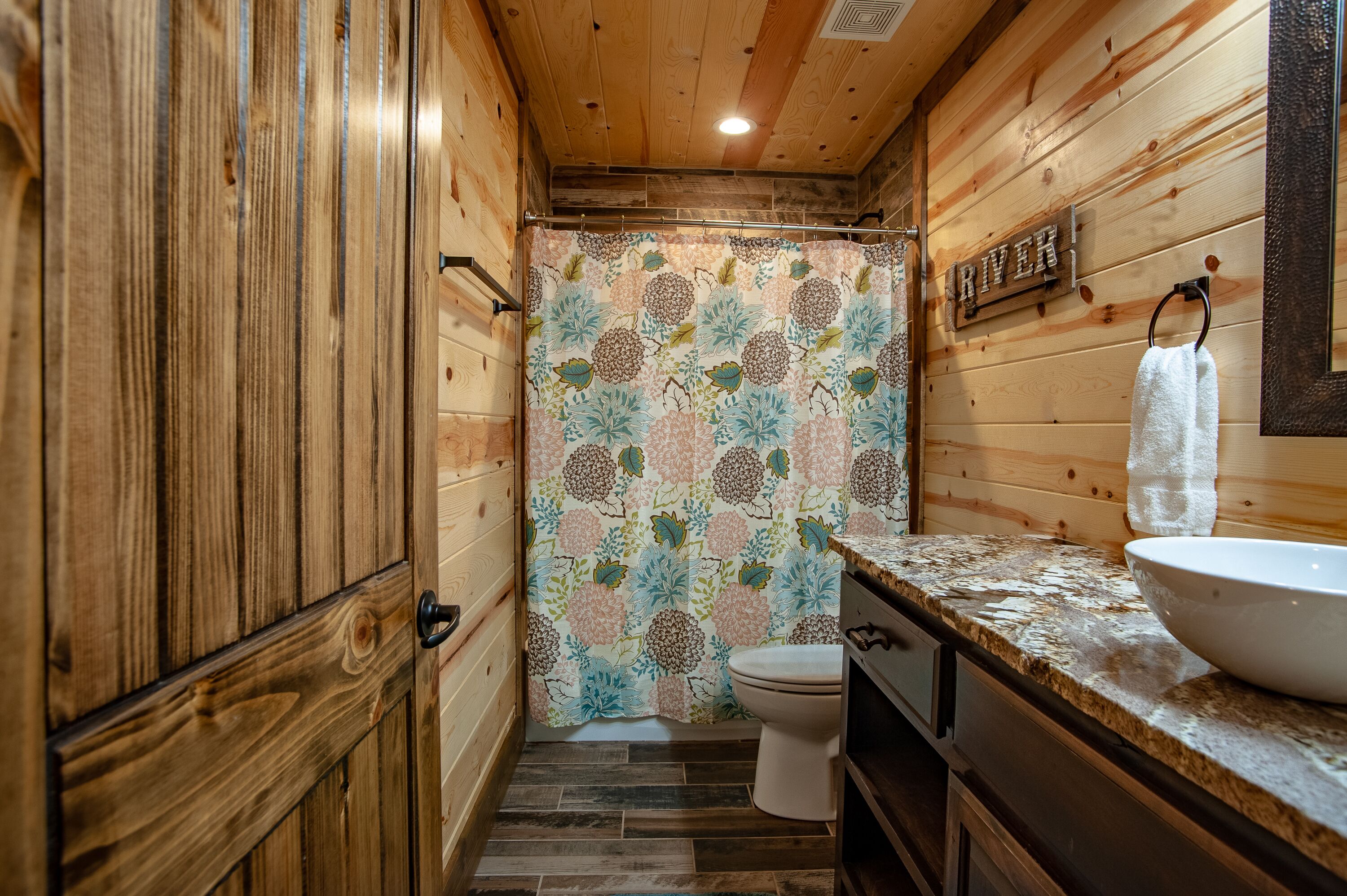Een houten badkamer met een toilet, wastafel en douchegordijn.