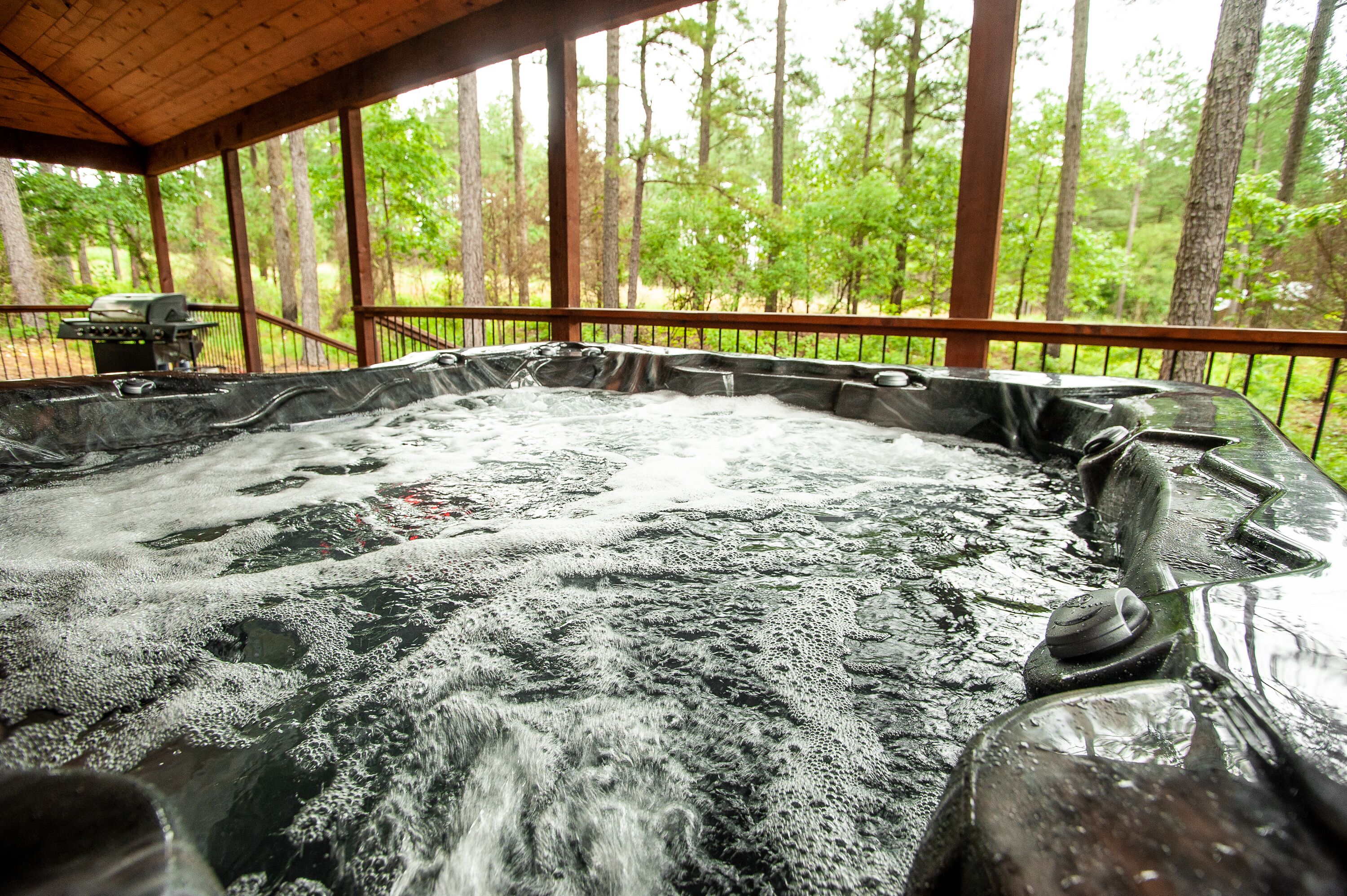 Un jacuzzi con terraza de madera y vista a un bosque.