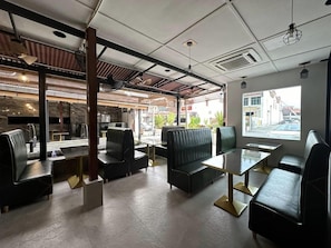 A modern indoor seating area with tables and booths, large windows, and a view of the street. - Banana Boutique Hotel (George Town)