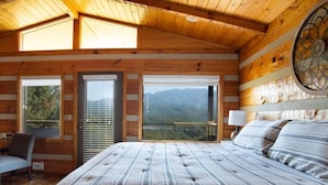 Un dormitorio con una cama grande, una silla, un escritorio y vistas a montañas a través de una ventana.