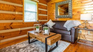 Ein gemütliches Blockhaus-Interieur mit Holzwand, Fenster mit Jalousien, einer Couch, einem Couchtisch mit Laternen und einem Spiegel mit Zierrahmen.