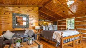 Ein Schlafzimmer in einer Holzblockhütte mit einem Holzbett, einem Sofa, einem Nachttisch und einem Spiegel.