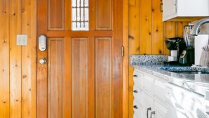 Une pièce aux murs lambrés, dotée d’une grande porte en bois, d’un coin cuisine avec des armoires blanches et des plans de travail en granit, et d’un petit tapis sur le sol.