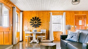 Une pièce chaleureuse aux murs en bois, avec une table à manger et des chaises, un canapé en cuir noir et une horloge murale originale.