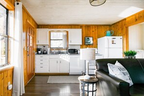 A cabin interior with a kitchen area, a dining table, and a black leather sofa.